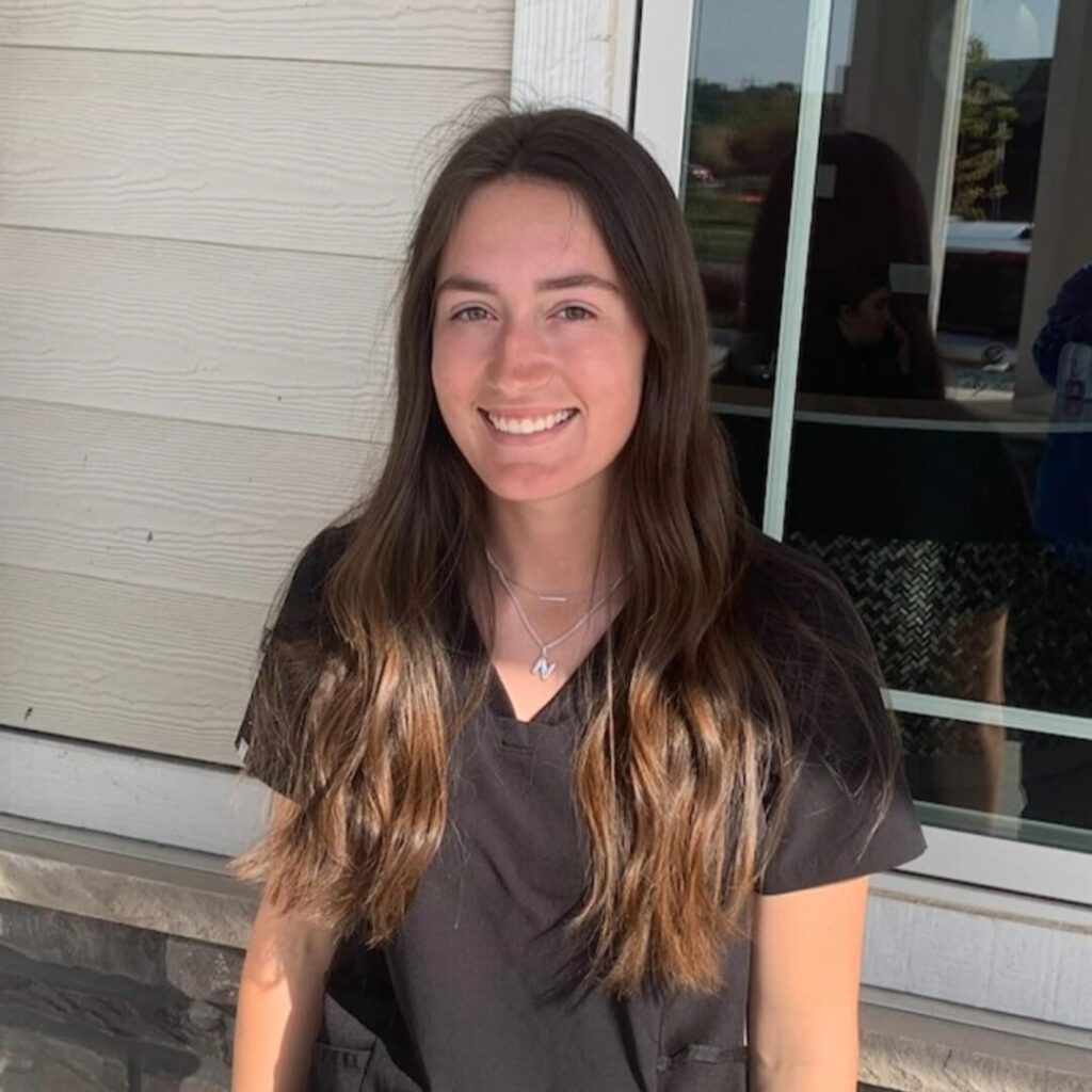 Female with long brown hair wearing black scrubs